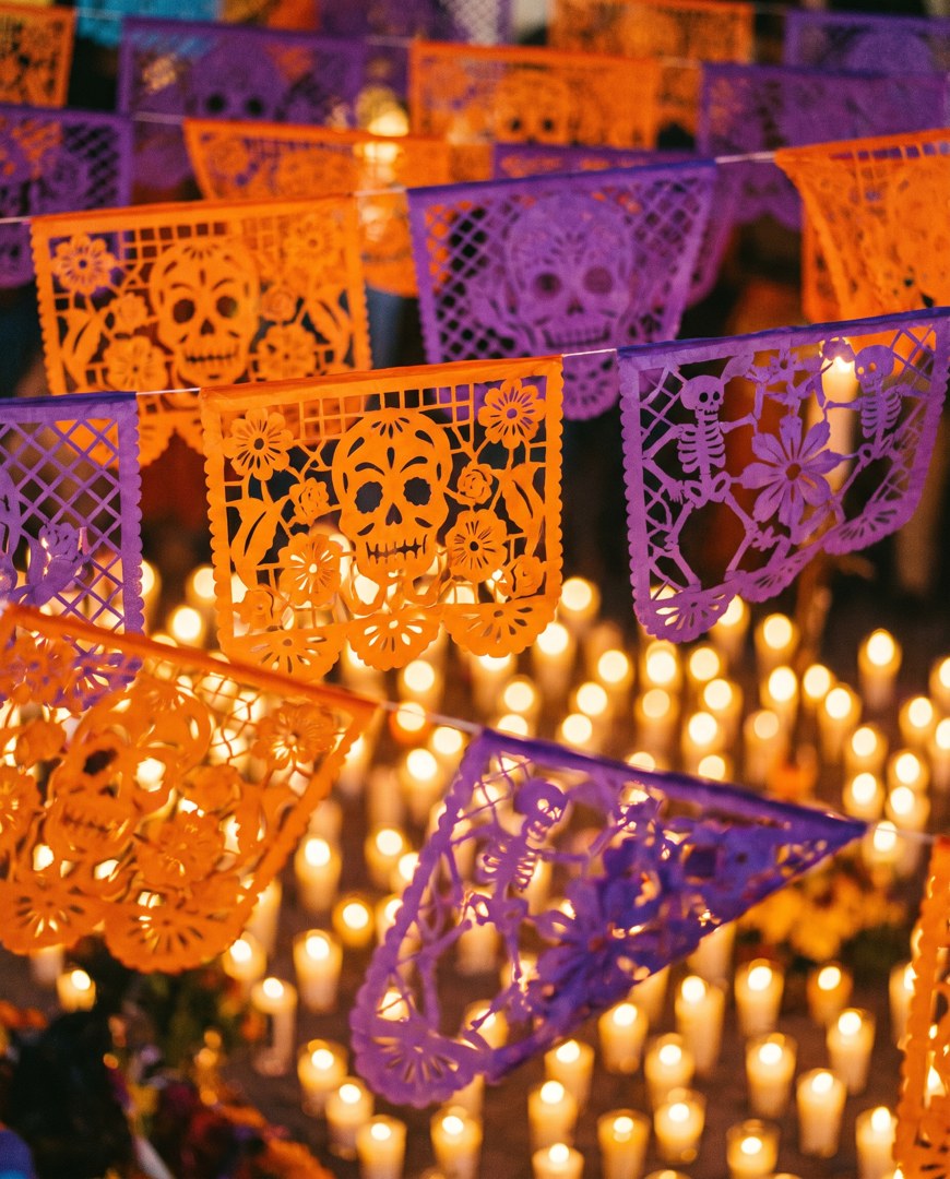 Velas encendidas bajo papel picado morado de Día de Muertos